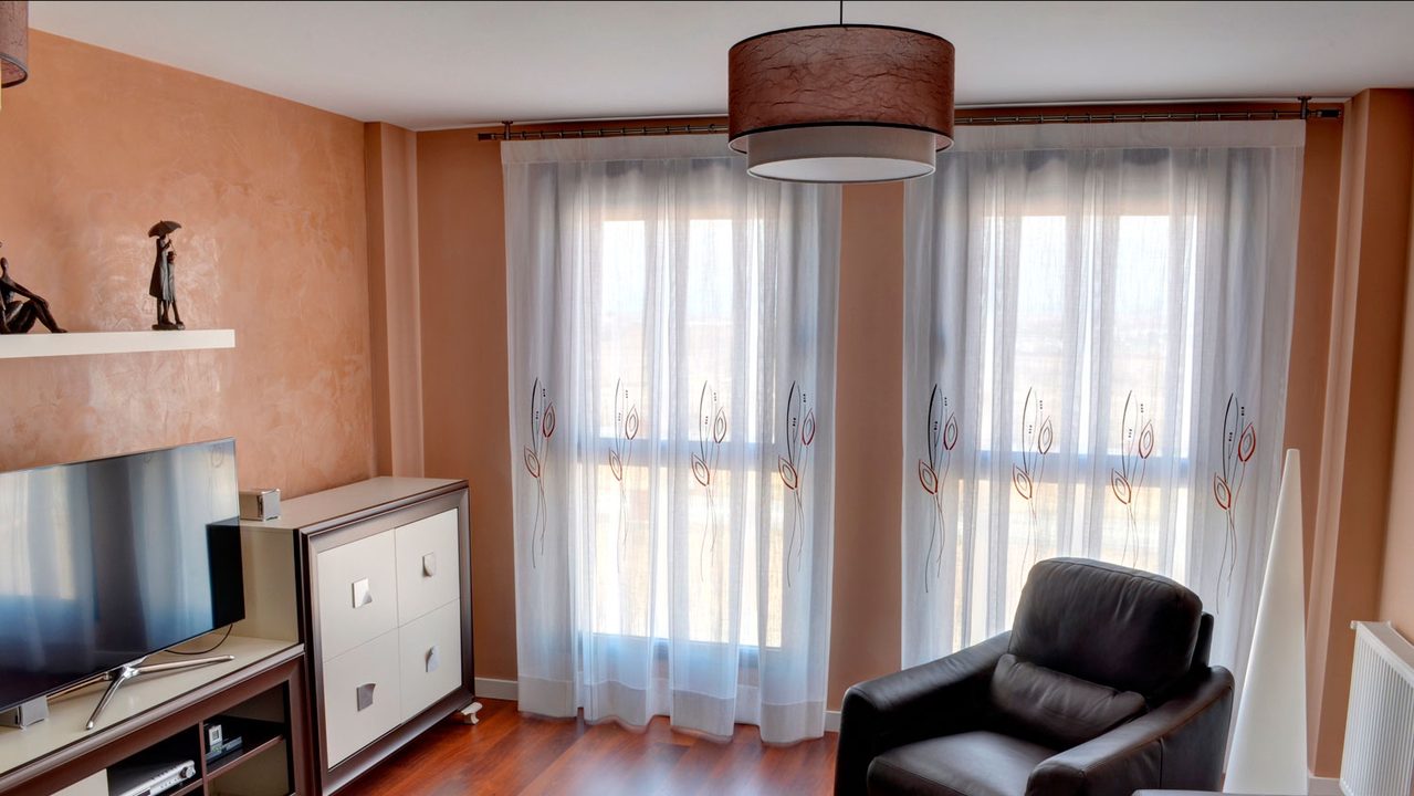 Visillos bordados de tablones en las dos ventanas de un salón