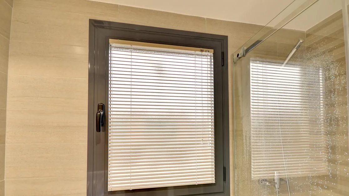 Ventana de un baño con una persiana veneciana de aluminio de colores base, de lamas de 25 mm