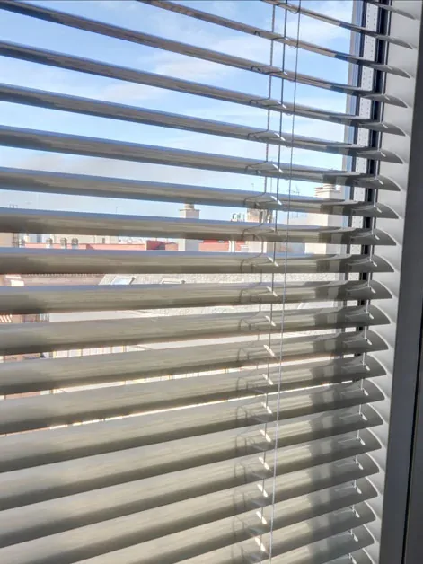 Lamas de aluminio de una veneciana vistas de cerca, con la escalerilla y el cordón