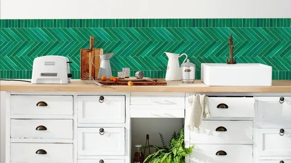 Cocina blanca con una franja de papel pintado verde en espiga sobre la encimera