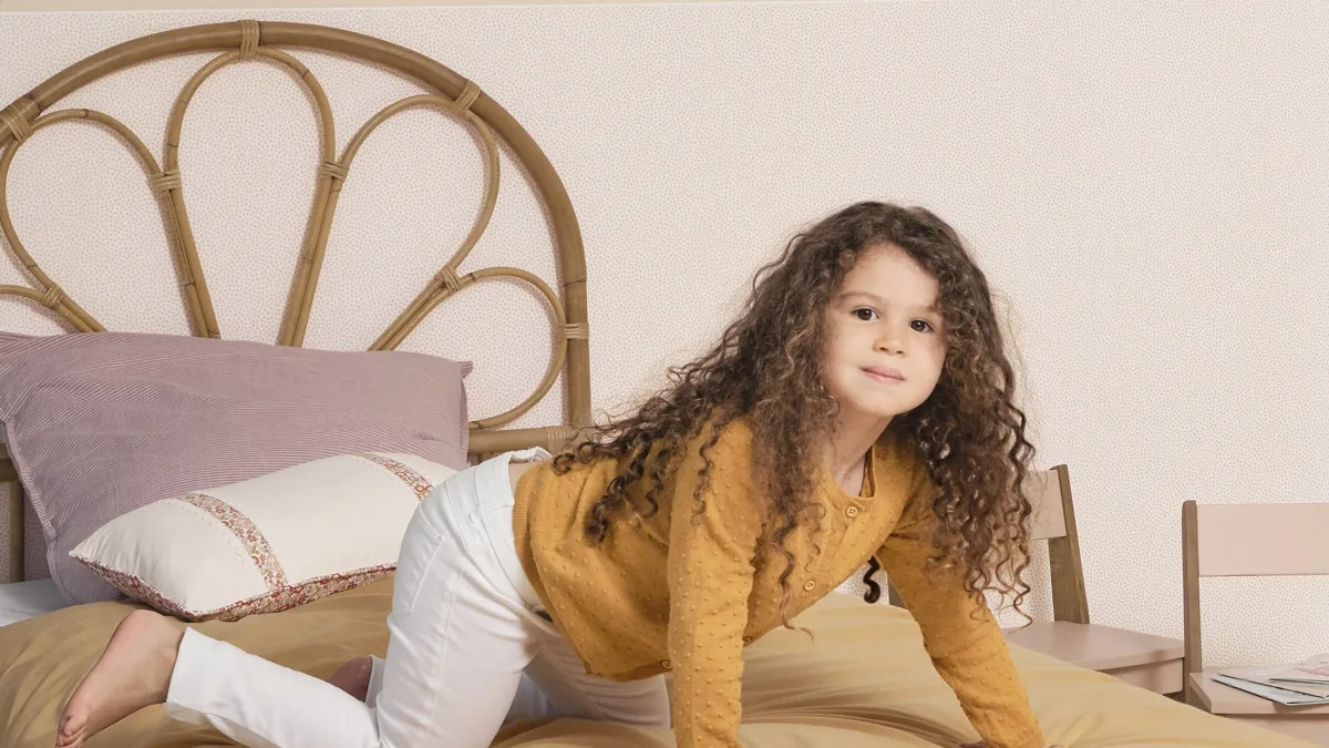Niña jugando en su cama delante de una pared con papel pintado infantil y cenefa