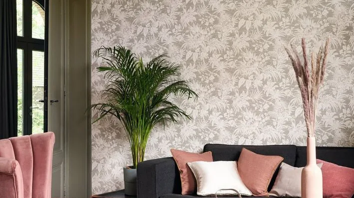 Salón con sofá negro y butaca rosa delante de una pared de papel pintado de hojas