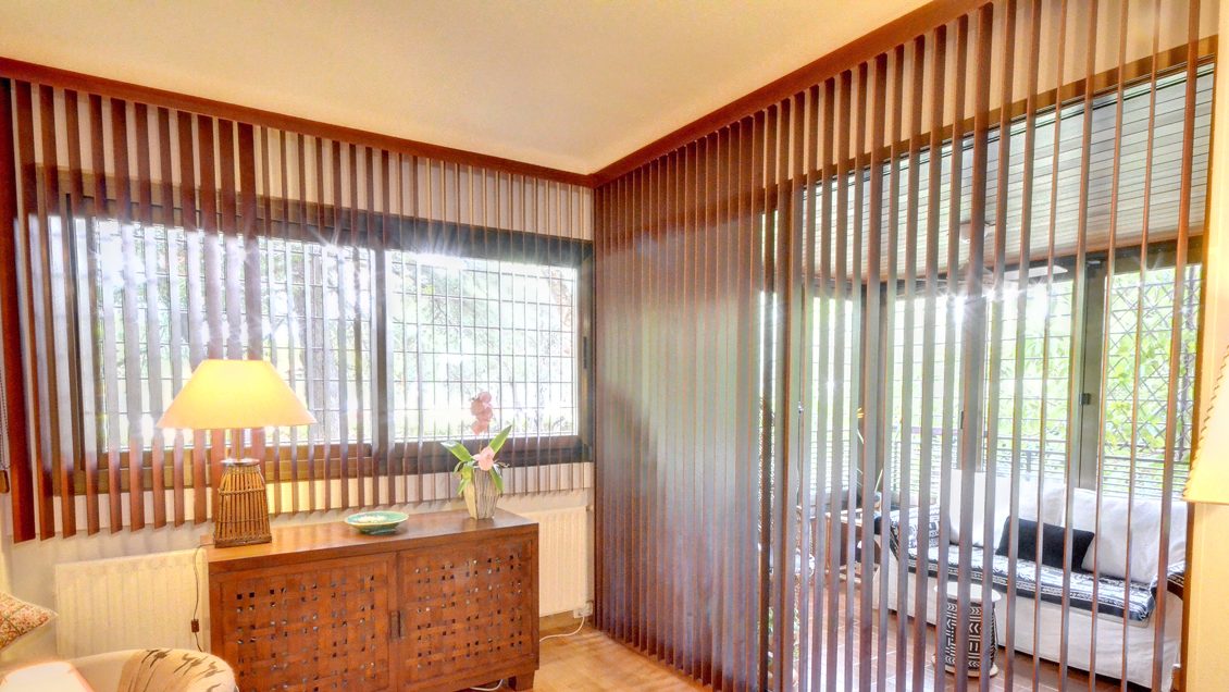 Salón con cortina vertical de madera en lamas abiertas sobre el ventanal