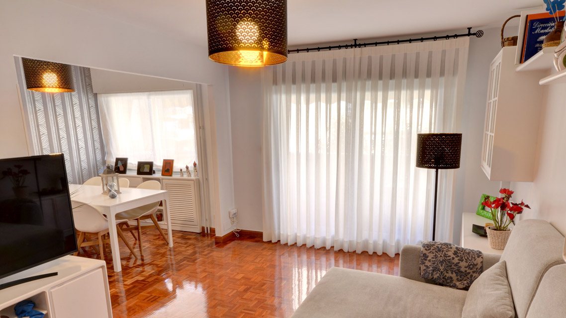 Salón con cortinas de tablas de lino blanco en barra de forja, sofá con chaise longue y comedor al fondo