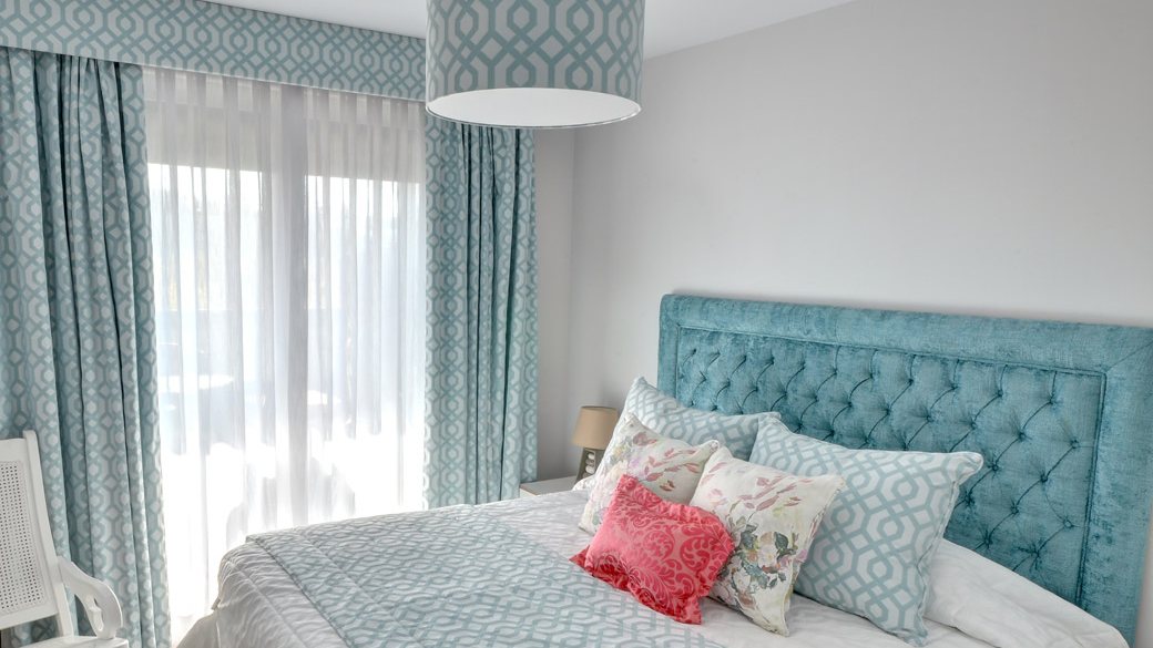 Dormitorio con cabecero capitoné tapizado en terciopelo turquesa, galería y lámpara tapizadas con la tela de las cortinas