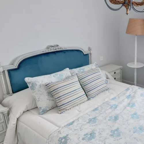 Cabecero de cama clásico tapizado en terciopelo azul, con cojines de rayas y colcha de flores
